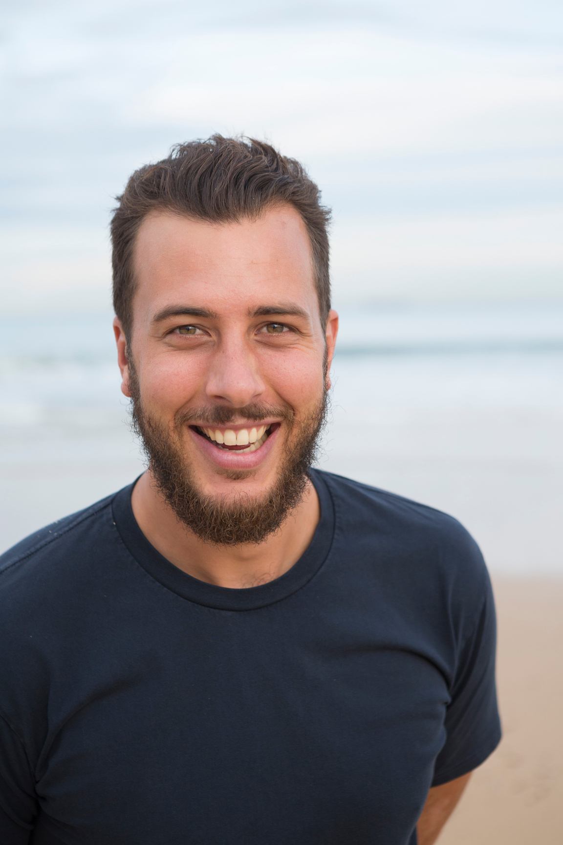a kind faced person with a beard and a blue shirt smiles at the camera